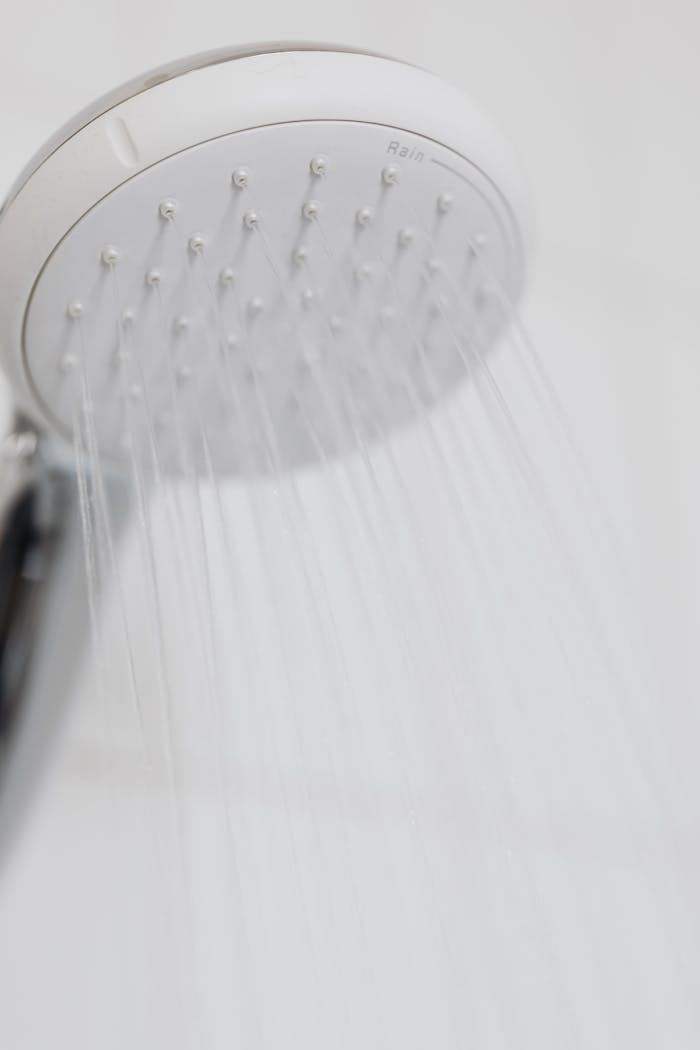 Close-up of a modern shower head with water streaming in a white bathroom setting.